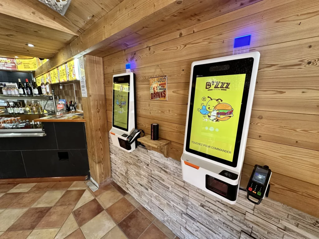 Deux bornes de commande iotill Kiosk et un terminal de paiement au comptoir d'un restaurant de burgers