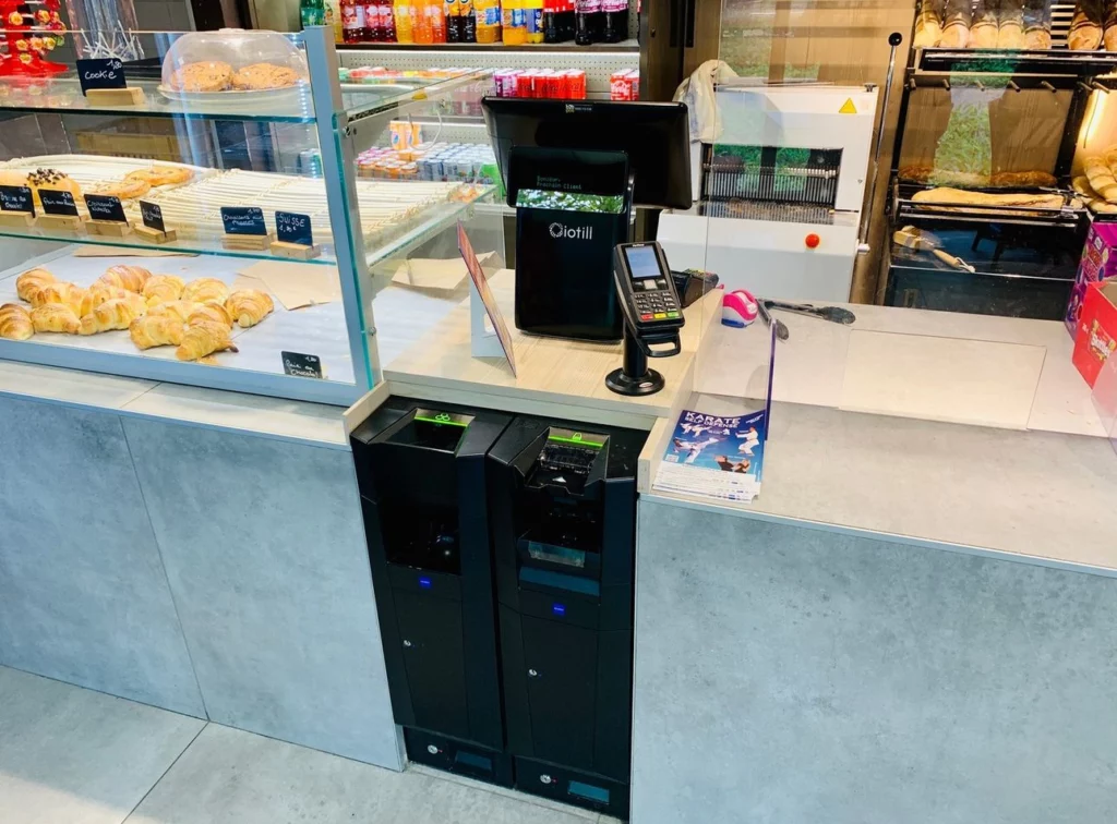 Comptoir de boulangerie équipé d'une caisse iotill et de deux monnayeurs automatiques intégrés sous le plan de travail.