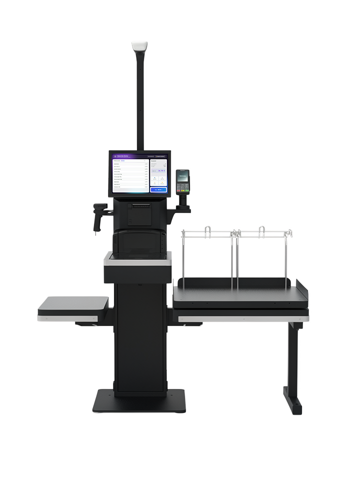 Caisse automatique iotill Self-Checkout : mât avec caméra et voyant de statut, écran tactile, scanner et douchette, imprimante, terminal de paiement, et zone de mise en sac avec plateau de pesée, porte-sacs et porte-panier.